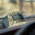 A Rural Def - Bottomland Edition Snapback Hat by Rural Cloth, featuring a black mesh back, rests on a car dashboard. The hat boasts a patch that reads, 