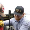 A man with a light beard is wearing an ACC Embroidered Hat by Rural Cloth, featuring the words 