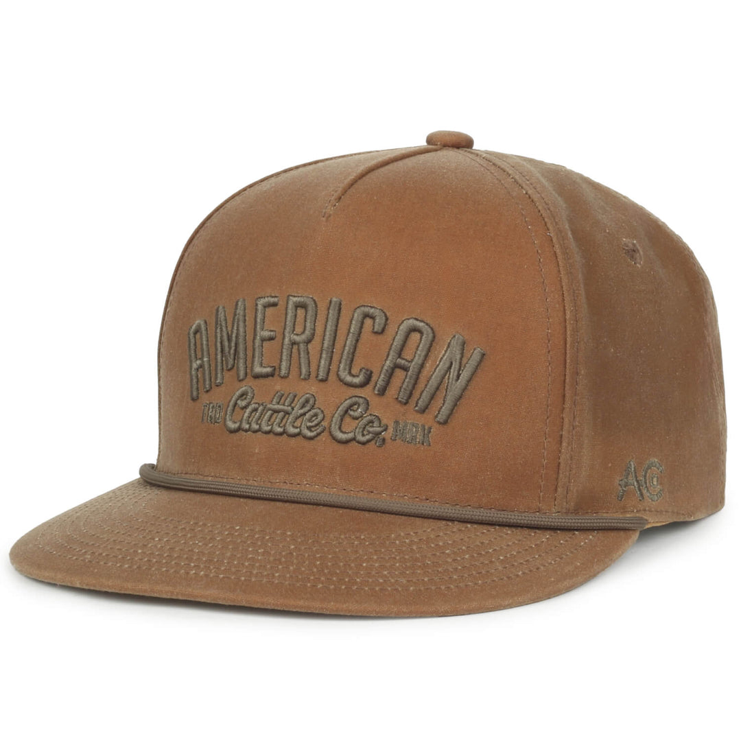 A Rural Cloth ACC Waxed Canvas hat, featuring a brown waxed canvas design with embroidered "American The Cattle Co., USA" text on the front. It comes with a curved brim, snapback closure, and an additional small emblem displaying the letters "AC" on the side.