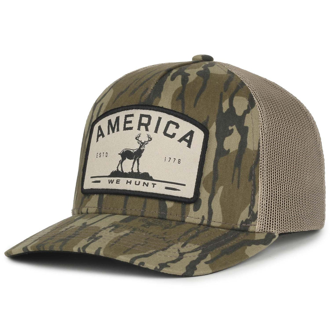 The America We Hunt Deer Hat - Bottomland by Rural Cloth is a camouflage baseball cap with a mesh back and snapback closure. It features a front patch that reads "AMERICA" at the top, "WE HUNT" at the bottom, and "ESTD 1776" on each side of a graphic of a deer. This good luck hat is perfect for any outdoor adventure.