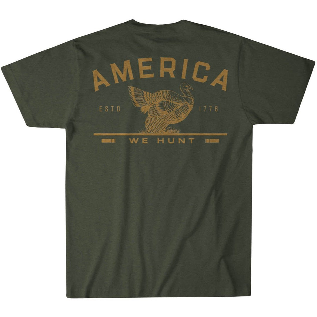 The America We Hunt Turkey Tee from Rural Cloth is a green t-shirt with a turkey hunting graphic in gold, "AMERICA" above, "ESTD 1776" on the sides, and "WE HUNT" below. Crafted from super soft cotton with premium weight fabric for rugged comfort, the rustic design is centered on the back.