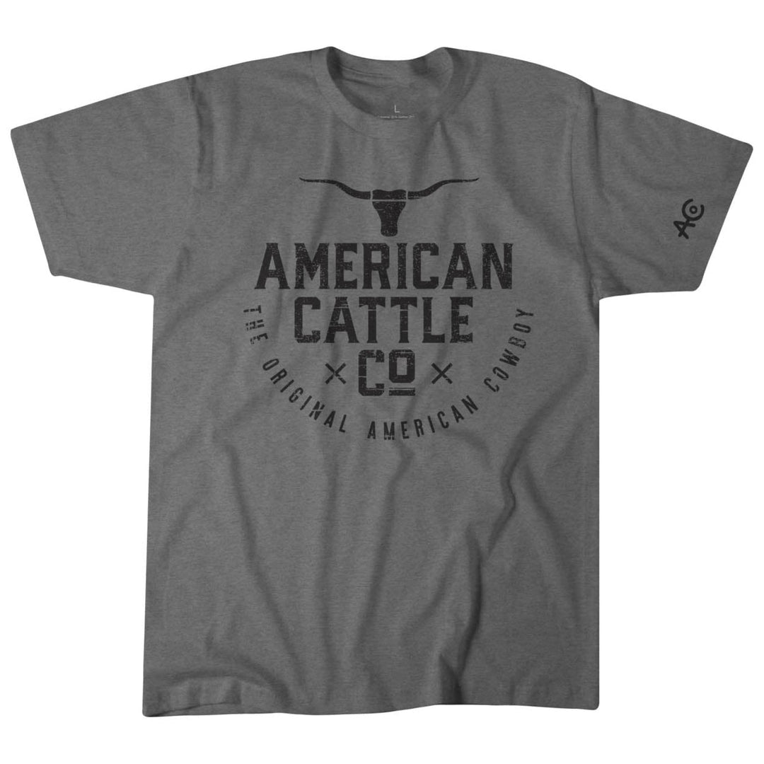 The American Cowboy Tee by Rural Cloth is a gray t-shirt with black text and graphics. "American Cattle Co." and a stylized longhorn skull stand out, accompanied by "The Original American Cowboy." Crafted from premium weight fabric, it features an emblem on the left sleeve. Made in the U.S.A.