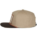 The Billboard Script Hat by 253408 is a beige baseball cap with a brown brim, showcasing a ranching vibe. It features a vintage patch on the front, has a round crown with ventilation eyelets, and includes a small rear tag labeled 