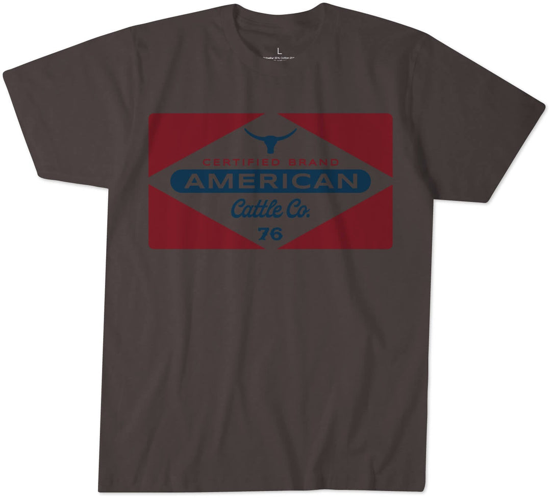 The Billboard Tee by Rural Cloth is a dark gray T-shirt made from super soft combed cotton. It features a large graphic on the front that includes a red diamond shape with a blue bull head at the top and the text "CERTIFIED BRAND AMERICAN Cattle Co. 76" in blue and red font inside the diamond.