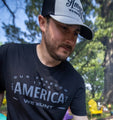 A man with a beard is wearing a black baseball cap and a black Hunt America Tee from Rural Cloth that reads 