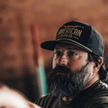 A person with a gray beard and mustache wearing a black Longhorn Hat with an embroidered 