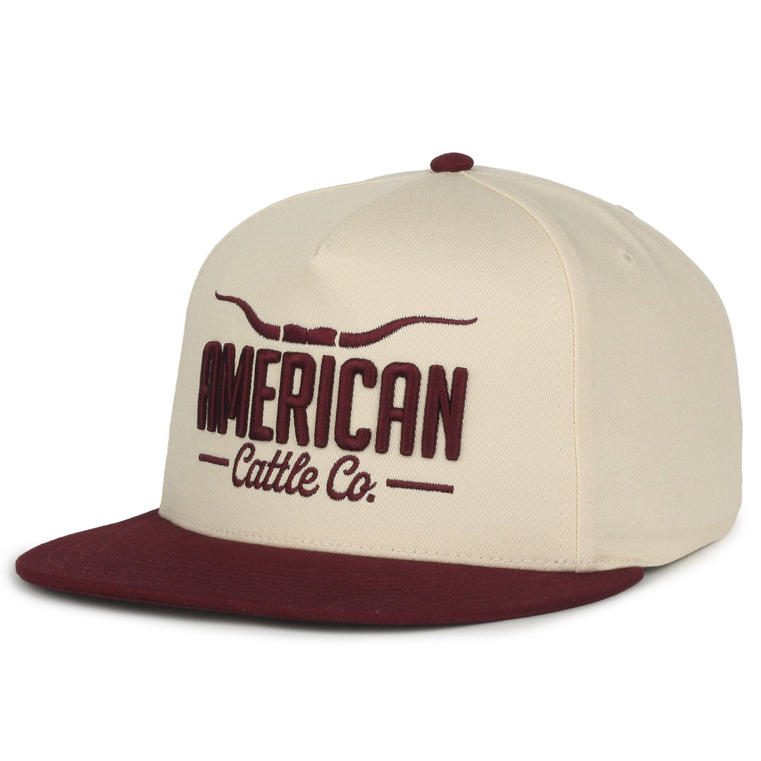 The Longhorn Hat - Solid from 269046 captures the cowboy spirit with cream and maroon tones. "American Cattle Co." is embroidered on the front beneath a stylized longhorn, featuring a maroon bill and button, ideal for anyone embracing the ranching lifestyle.
