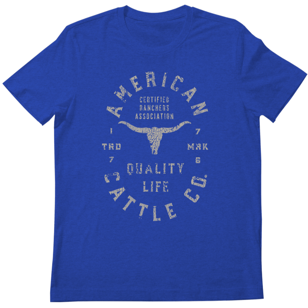 The Royal blue Quality Tee from Rural Cloth features a distressed graphic design. The white text reads "American Cattle Co. Certified Ranchers Association. Quality Life. Trademark 1776." A bull skull silhouette is prominently displayed in the center, celebrating the legacy of American ranching in this premium t-shirt.