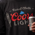 A close-up shows a person holding a can of Coors Light beer, dressed in a black 