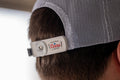 A person wearing a white mesh baseball cap fitted with the RC x CL SNAPS Bottle Opener from Rural Cloth, designed as a bottle opener on the back. The clip, featuring the Coors Light logo in red and gray, is perfect for enjoying longneck drinks.