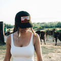 A woman wearing a white tank top and a black adjustable Sunrise Hat with the 