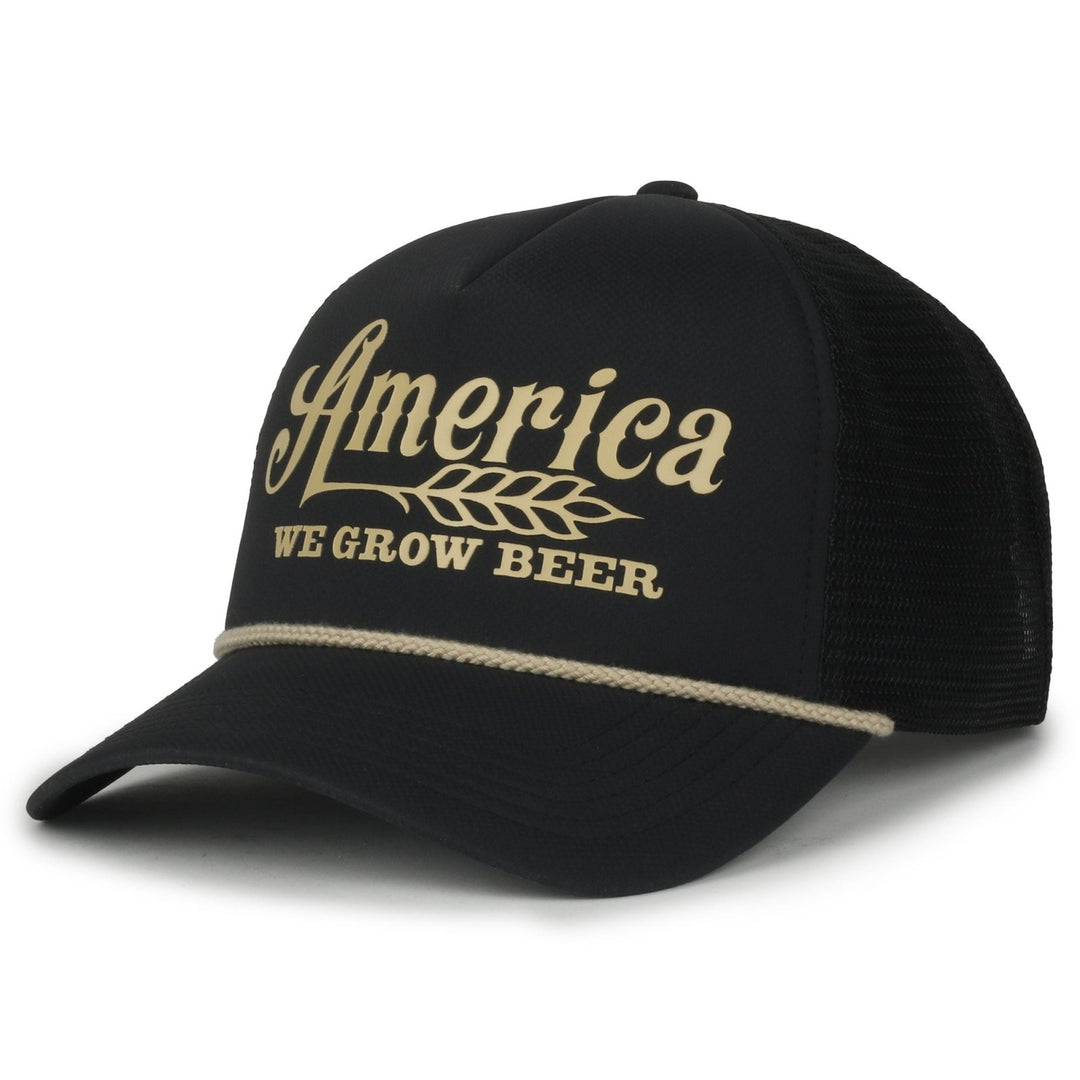 The We Grow Beer Foamie by Rural Cloth is a black mesh snapback hat featuring a mesh back and white rope detail above the brim. The front showcases "America" in a stylized font alongside a wheat graphic, with the phrase "WE GROW BEER" boldly displayed below, embodying the spirit of rural American pride.