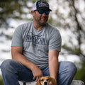 A man wearing sunglasses, a blue and white 'We Grow Beer' hat with an adjustable snapback closure from Rural Cloth, and a gray t-shirt with the word 