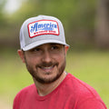 A man with a beard is wearing a red shirt and a Rural Cloth We Grow Beer Hat-Gray, which features a patch that reads 