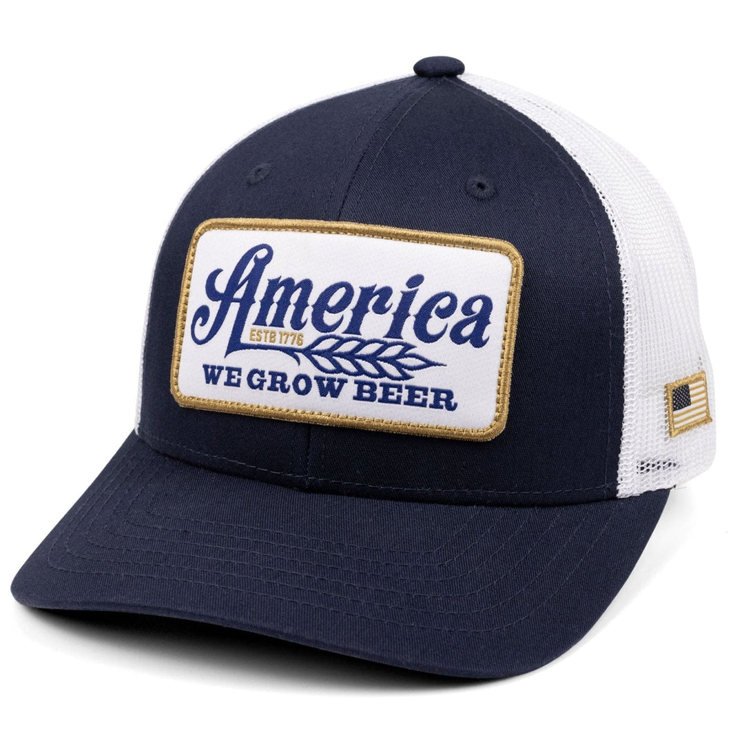 The "We Grow Beer Hat-Less Filling!" by Rural Cloth is a navy blue and white mesh baseball cap, adorned with a logo patch that reads "America ESTB 1776 WE GROW BEER." This tribute to American pride also features a small American flag patch on the side.