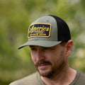 A man wearing Rural Cloth's We Grow Beer Hat-Olive, featuring an olive green and black design with a yellow and black patch stating 