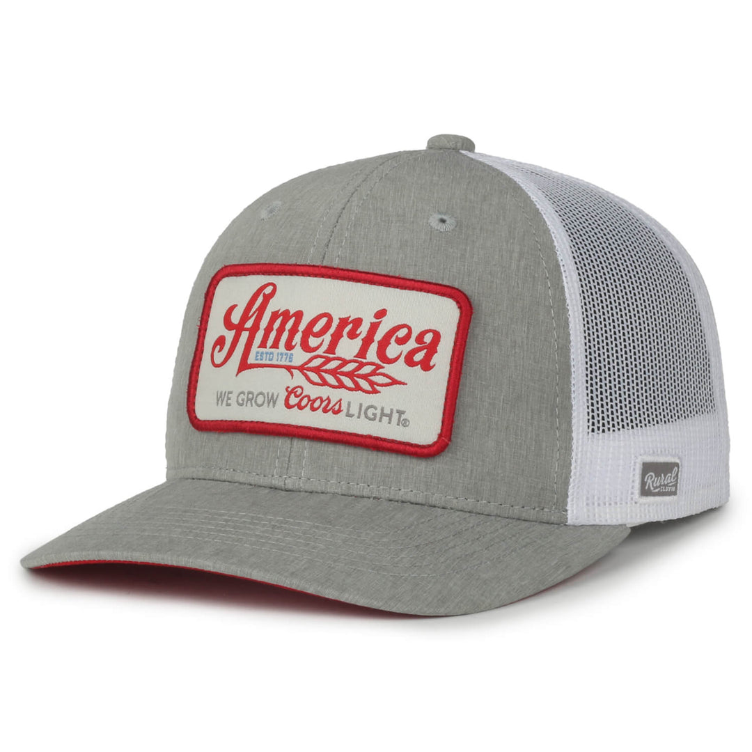 The We Grow Coors Light Hat by Rural Cloth is a grey and white trucker hat that features a rectangular patch on the front with "America" emblazoned in large red letters, followed by smaller text saying "We Grow Coors Light." This American beer hat boasts a mesh back and a grey bill with a red underside.