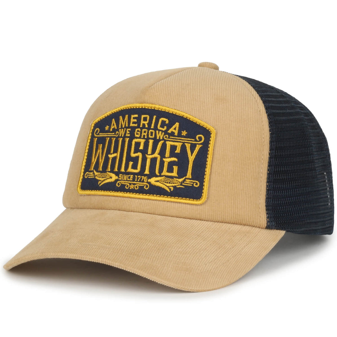 Introducing the We Grow Whiskey Hat-Corduroy by Rural Cloth – a stylish tan and black snapback featuring a yellow patch with "America We Grow Whiskey Since 1776" embroidered in dark blue. The front showcases premium tan corduroy, complemented by a black mesh back and bill for an effortlessly cool look.