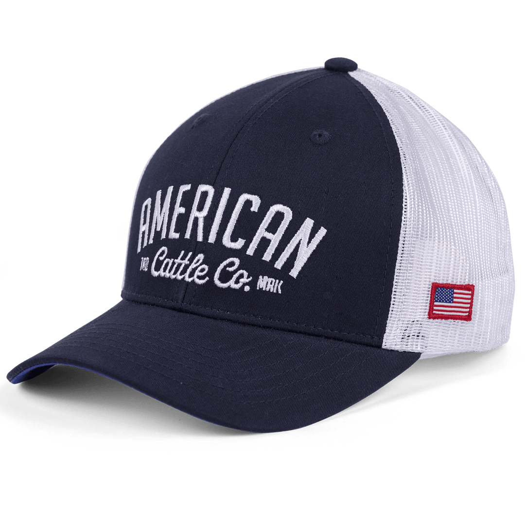 The ACC Embroidered Hat by Rural Cloth features a navy front and white mesh back, with an adjustable snapback closure. The front is adorned with "AMERICAN Cattle Co." in white text, and an American flag patch is sewn on the left side, combining style and functionality into this attractive American Cattle Company hat.