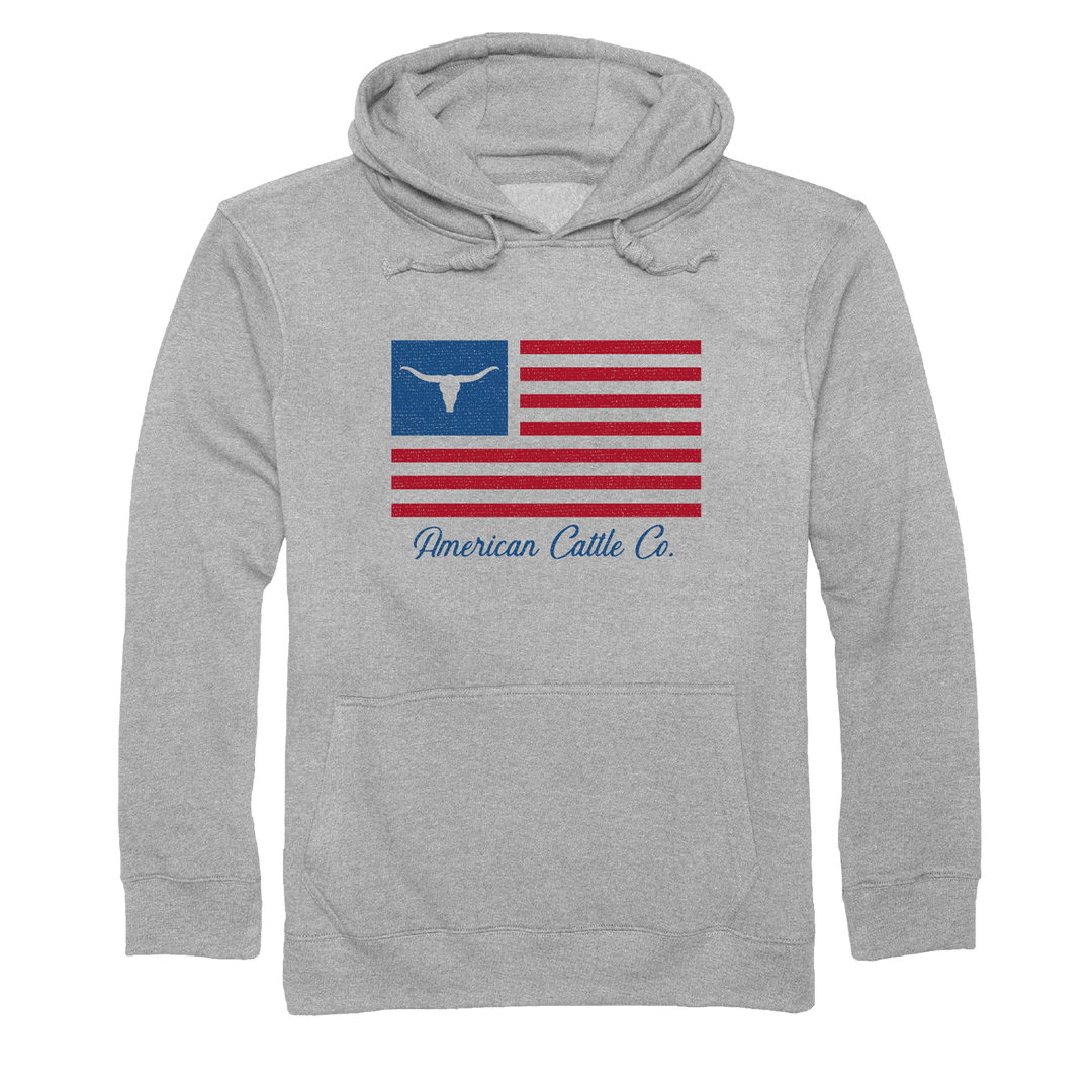 The ACC Flag Pullover-Gray by Rural Cloth is a gray hooded sweatshirt featuring a graphic on the front. The design includes the American flag with a blue field and white cattle horn where stars typically are, evoking American cattle ranching, and "American Cattle Co." written in blue script below the flag.