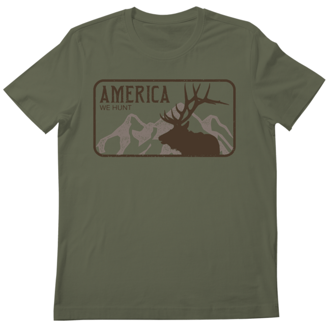 The America We Hunt Elk Tee in Military Green Frost by Rural Cloth showcases a striking large elk graphic with antlers set against a mountainous backdrop. The bold text "AMERICA WE HUNT ELK" is positioned above the elk, and the rectangular design is centered on the chest area of this hunting t-shirt.