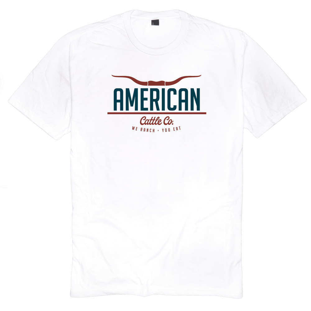 The American Cattle Co Tee by Rural Cloth showcases the text "American Cattle Co." with an illustration of longhorn cattle horns above it, capturing the essence of the American lifestyle. Below, it features the tagline, "We Ranch - You Eat." The text is primarily in teal and red colors.
