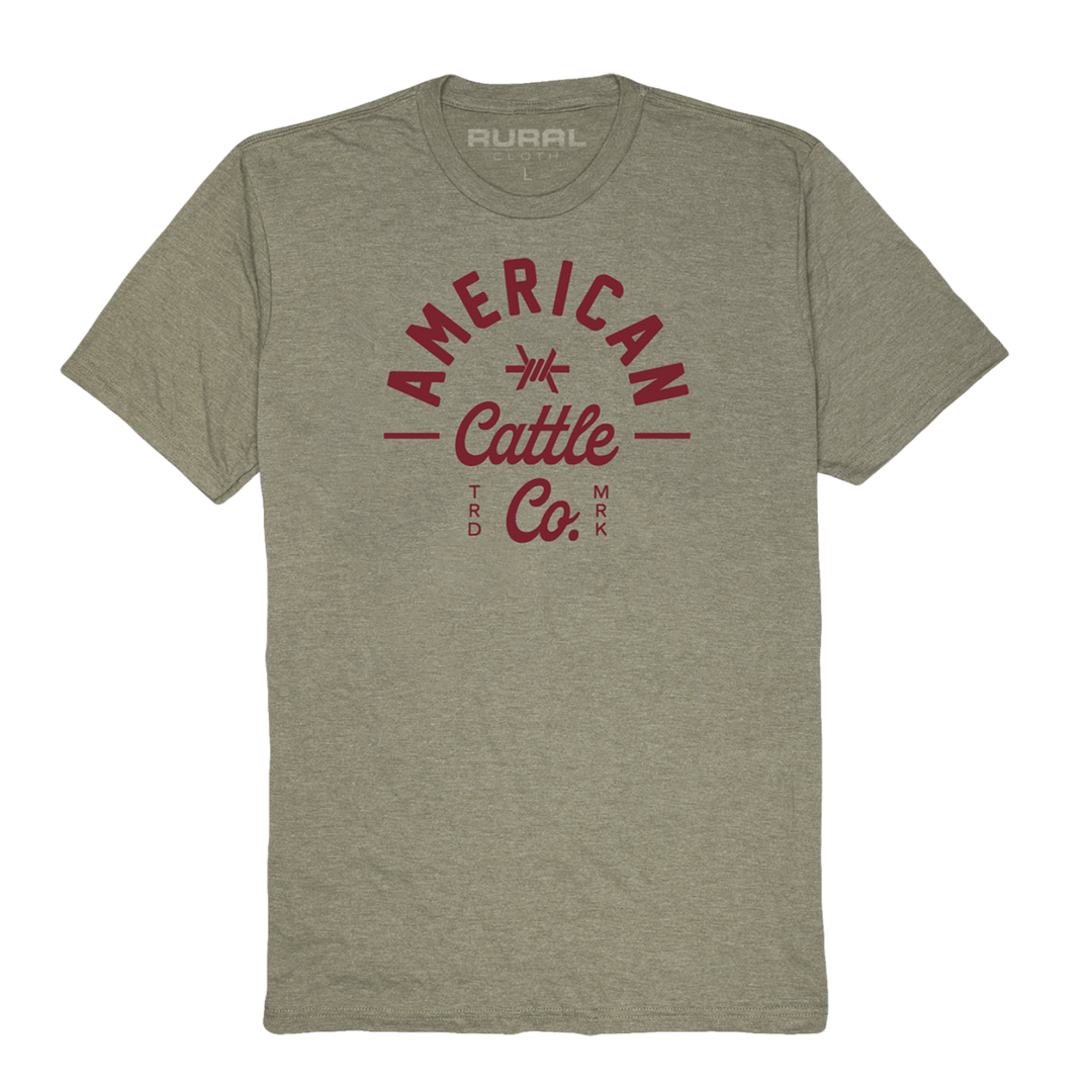 Introducing the Barb Tee by Rural Cloth: a light gray t-shirt crafted from premium weight fabric, featuring "American Cattle Co." in bold red letters on the front. The design is accented with small red decorative lines resembling barbed wire, and the word "Rural" is printed near the neckline.