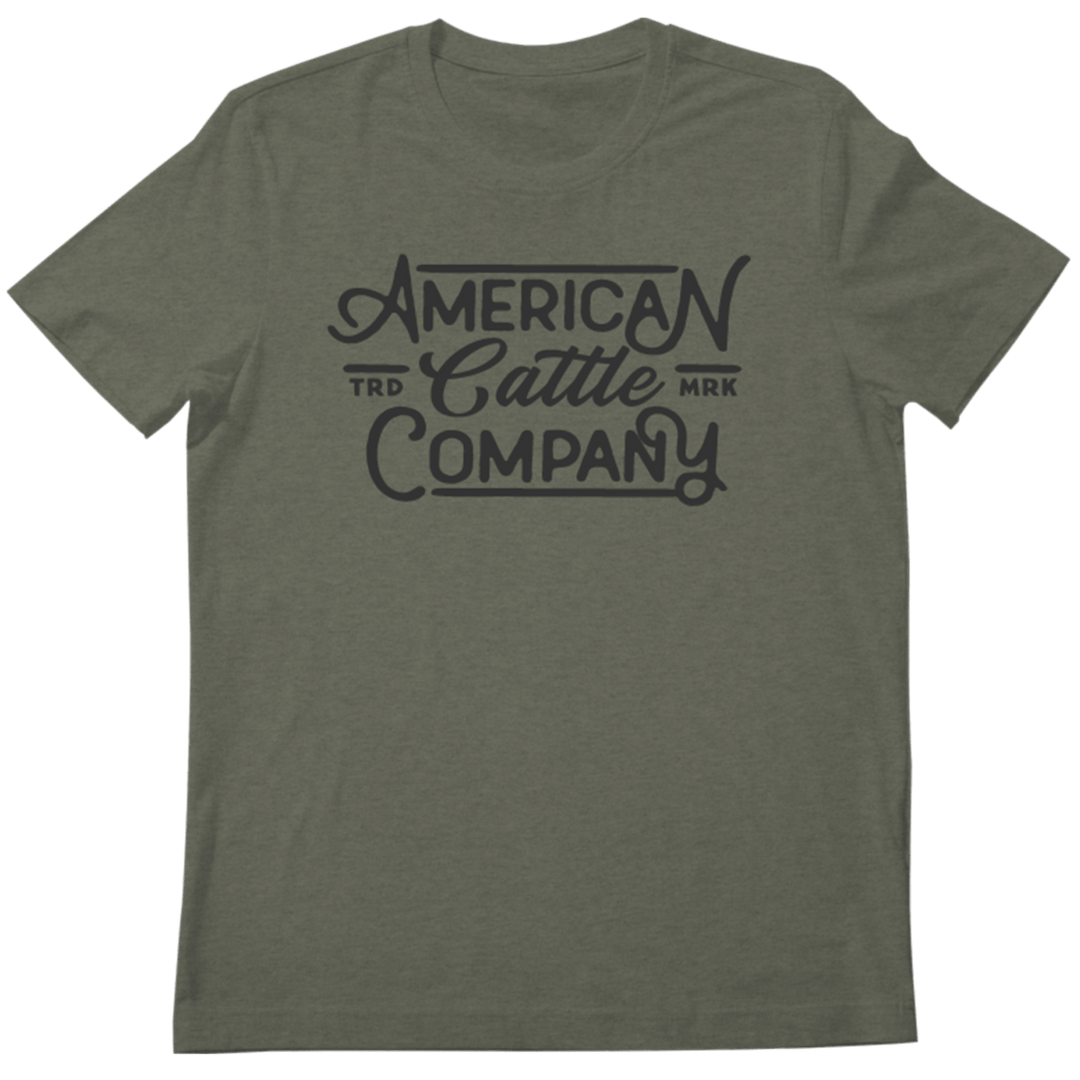 The Billboard Script Tee by Rural Cloth is a green short-sleeve t-shirt featuring dark blue text that reads "American Cattle Company," with smaller words "TRD" and "MRK" flanking "Cattle," embodying the spirit of American ranching.