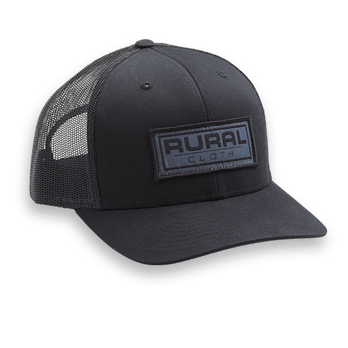 The Brandmark Hat by Rural Cloth is a stylish accessory that features a black design with a breathable mesh back and an embroidered patch on the front displaying "Rural Cloth." This hat also comes with an adjustable snapback for a perfect fit.