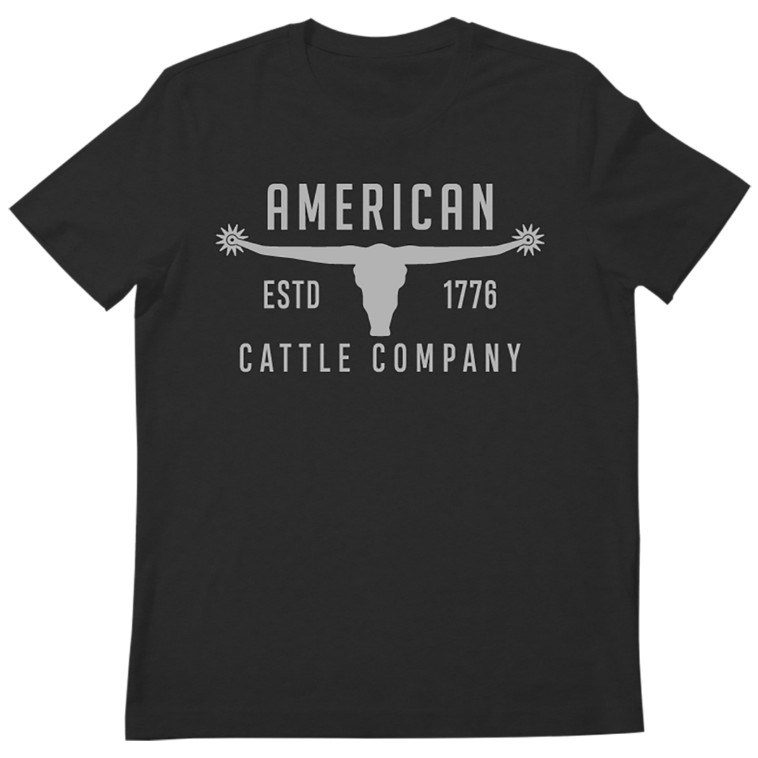 The "Bull Spurs Tee-Black Frost" by Rural Cloth is a black T-shirt showcasing a white graphic of a longhorn skull with starburst decorations, evoking Western symbolism. The design includes the text "AMERICAN CATTLE COMPANY" above and "ESTD 1776" below, framing the skull on high-quality premium weight fabric.