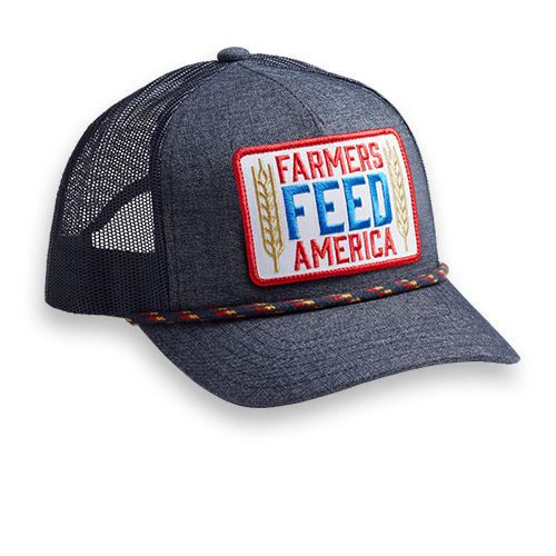 The Farmers Feed America Hat by Rural Cloth is a black trucker style hat featuring a rectangular patch with the slogan 
