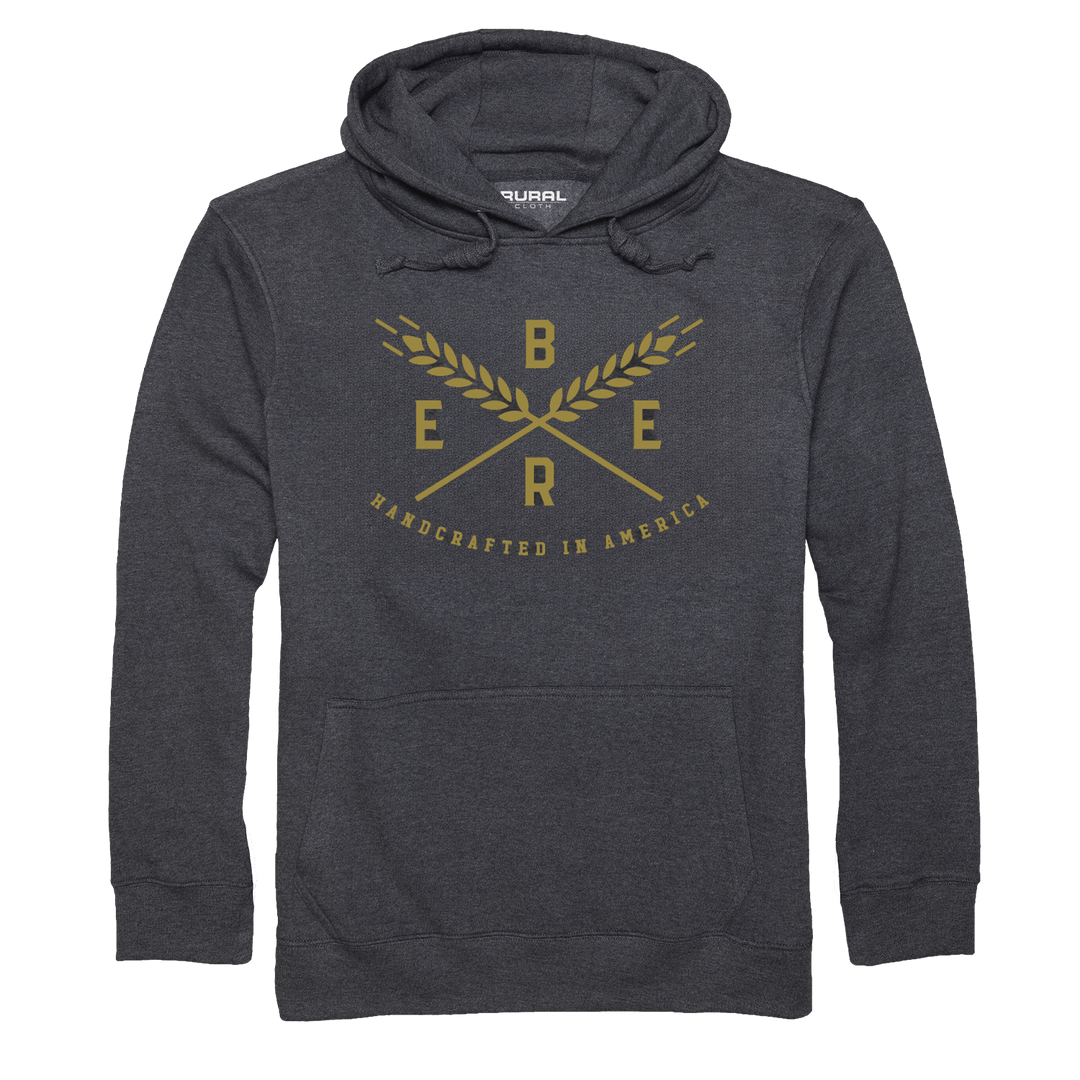 Introducing the Handcrafted Pullover-Charcoal Heather by Rural Cloth: a dark gray hoodie with drawstrings and a front pocket. The front showcases a gold design featuring crossed wheat stalks, the letters "B," "E," "E," and "R" between them, and the text "HANDCRAFTED IN AMERICA" underneath. Made from premium materials, it celebrates American beer crafting heritage.