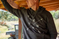 A person wearing a charcoal heather Hunt Pullover hoodie by Rural Cloth, featuring crossed arrow graphics labeled 