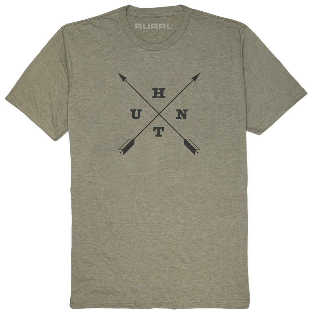 The Military Green Frost Hunt Tee from Rural Cloth showcases the word "RURAL" printed inside the collar. The front of this adventure clothing piece features a black graphic with two crossed arrows forming an "X" shape, each quadrant containing one letter: U, H, N, T.
