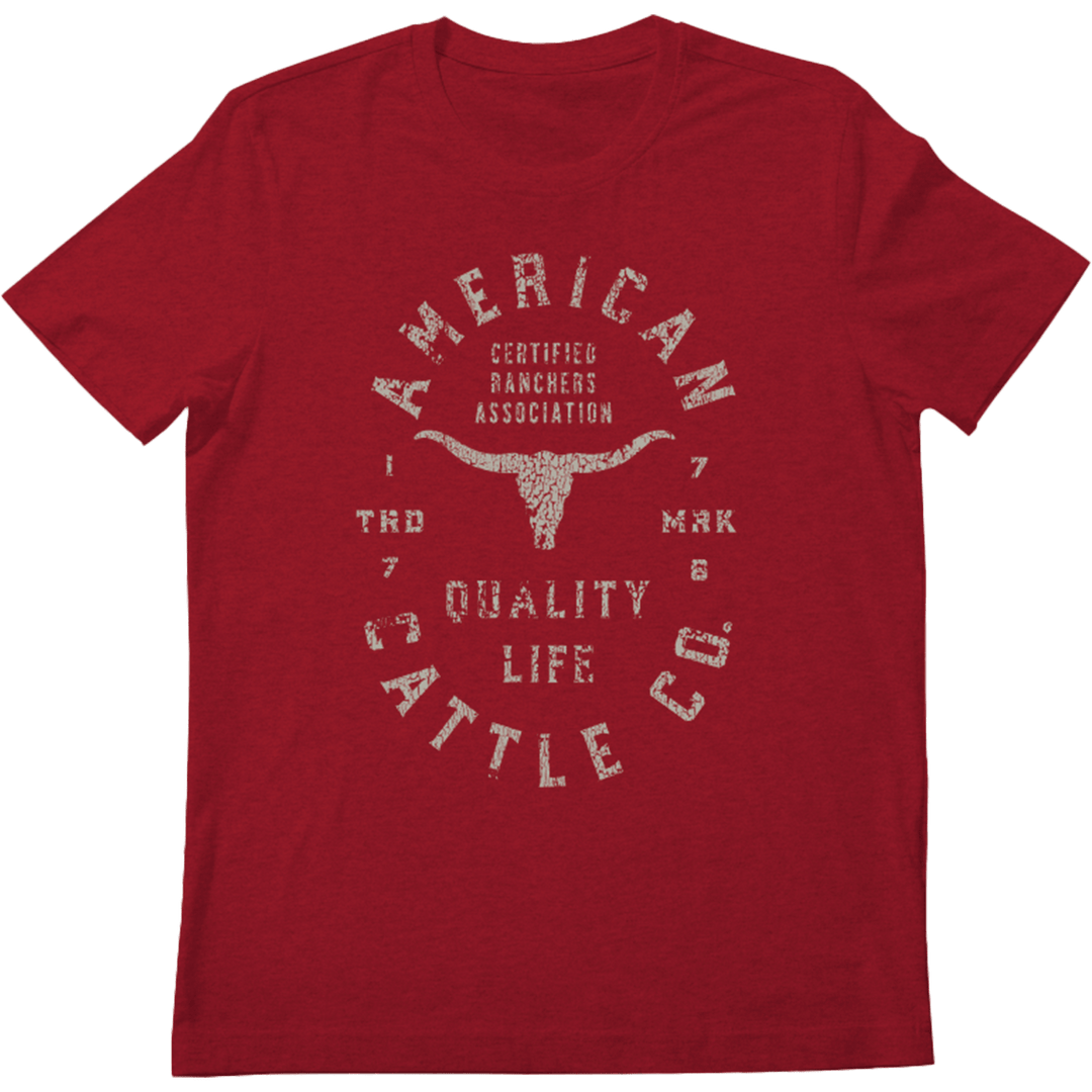 The Quality Tee by Rural Cloth is a red T-shirt that showcases a vintage-style design with white distressed text. The design reads "American Cattle Co." and includes "Certified Ranchers Association," "Quality Life," and the years "1776" and "1786" encircling a graphic of a longhorn skull, celebrating American ranching heritage.