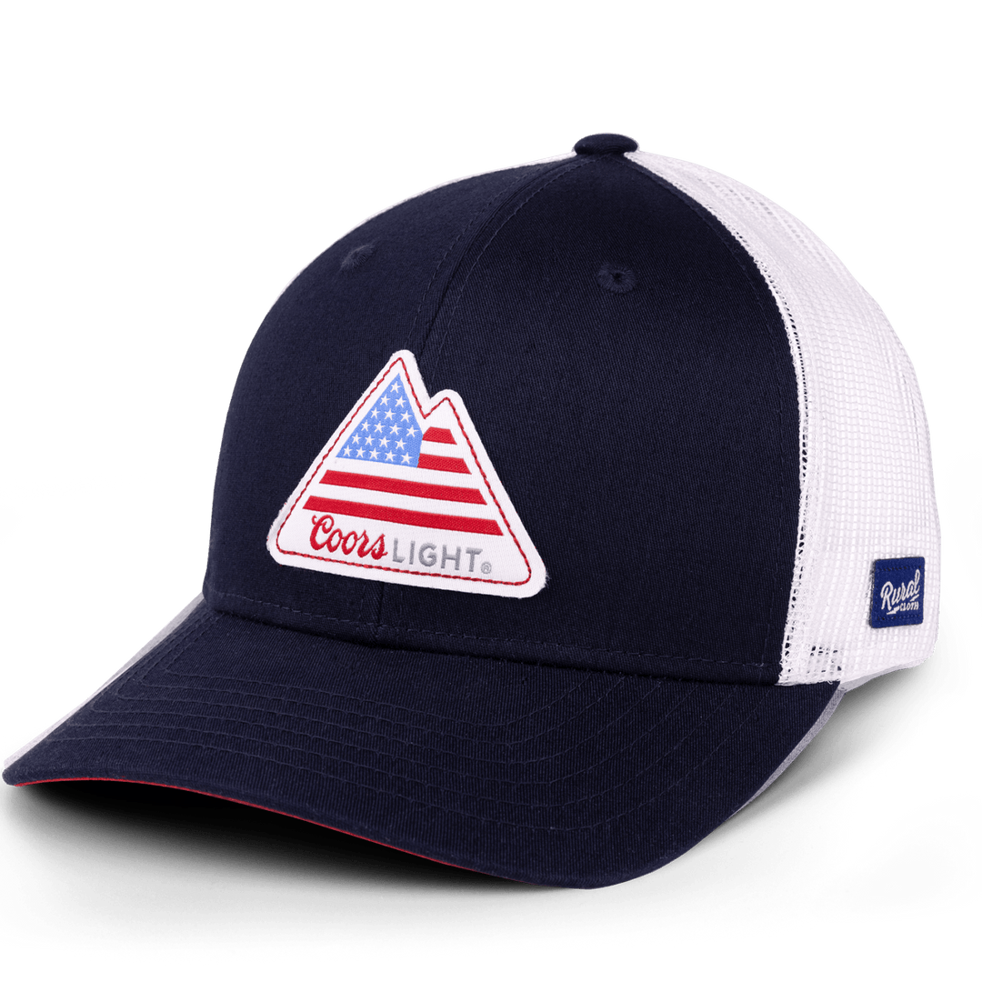 The Rocky Mountain Flag Hat from Rural Cloth is a black and white trucker cap featuring a "Coors Light" logo on the front. The iconic Silver Bullet logo includes a triangular design with an American flag pattern. The hat has a black front panel and bill, with white mesh at the back and sides, making it perfect for fans of this classic American beer.
