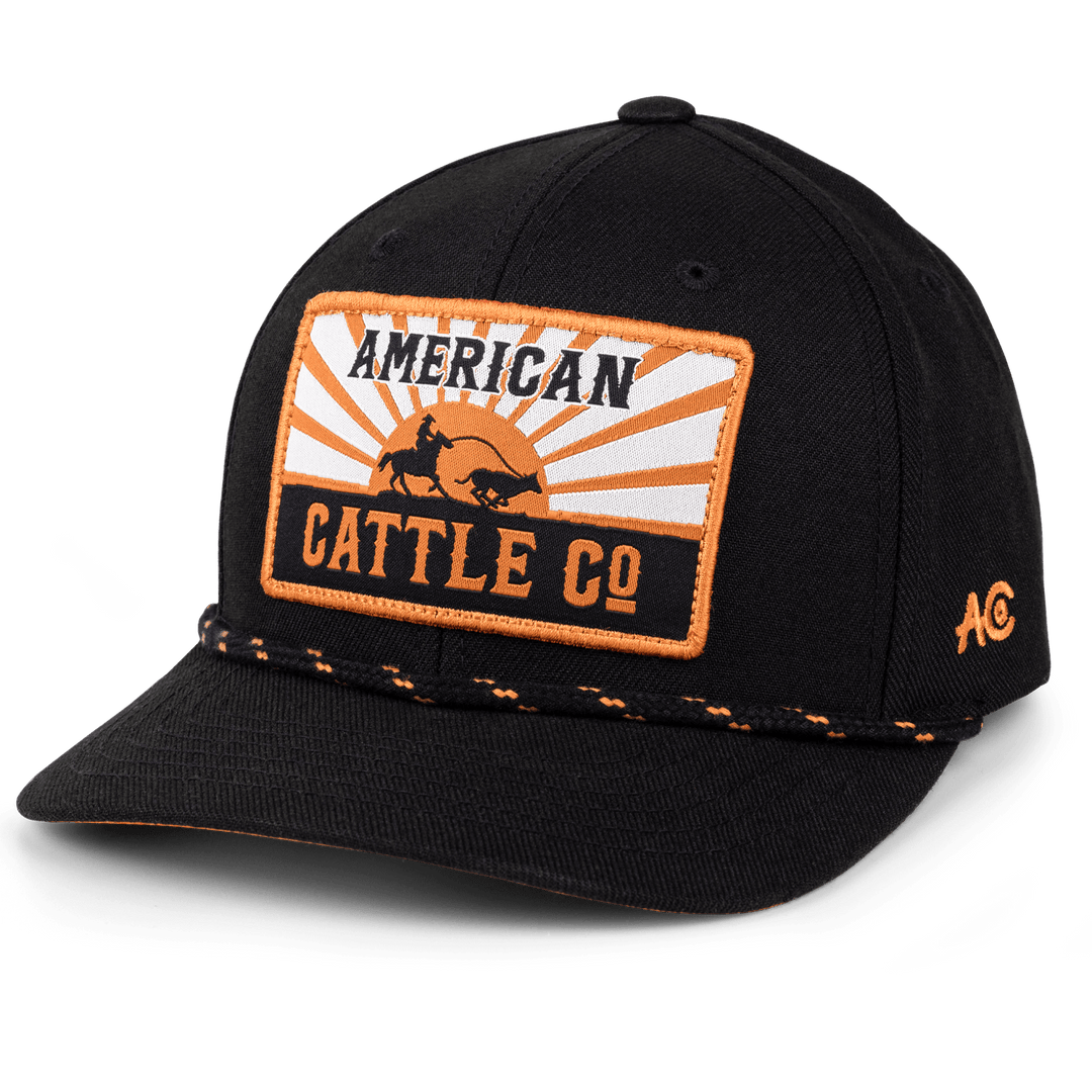 Introducing the Sunrise Hat by Rural Cloth: a stylish black baseball cap featuring a rectangular patch on the front. The patch showcases an orange and white design with the text "American Cattle Co" alongside an illustration of cattle. The cap also sports an orange and black braided rope above the brim, an "AC" logo on the side, and comes with an adjustable snapback closure for a perfect fit.