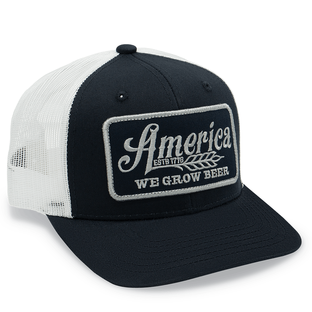 The Rural Cloth "We Grow Beer Hat-Blue/White" is an American-made trucker hat featuring a patch that reads "America Estb 1776 We Grow Beer" on the front. The hat showcases a blue brim, white front panel, and mesh back for a classic look. It also includes an adjustable snapback to ensure the perfect fit.