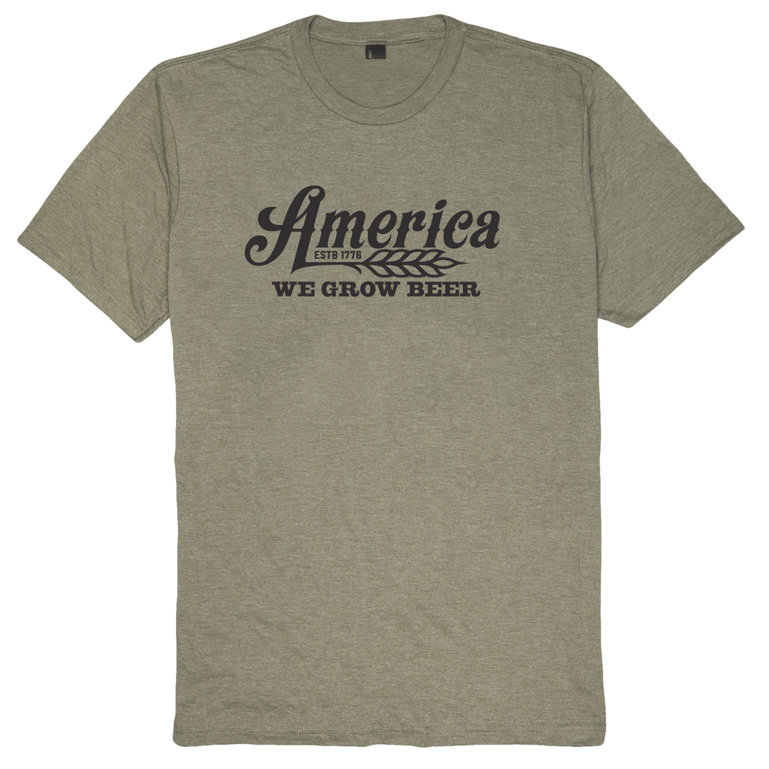 The We Grow Beer-Military Green Frost by Rural Cloth is a military green T-shirt crafted from super soft combed cotton. It features the text "America ESTD 1776 WE GROW BEER" in black letters along with a wheat graphic between "America" and "We Grow Beer." Its modern athletic fit ensures ultimate comfort.