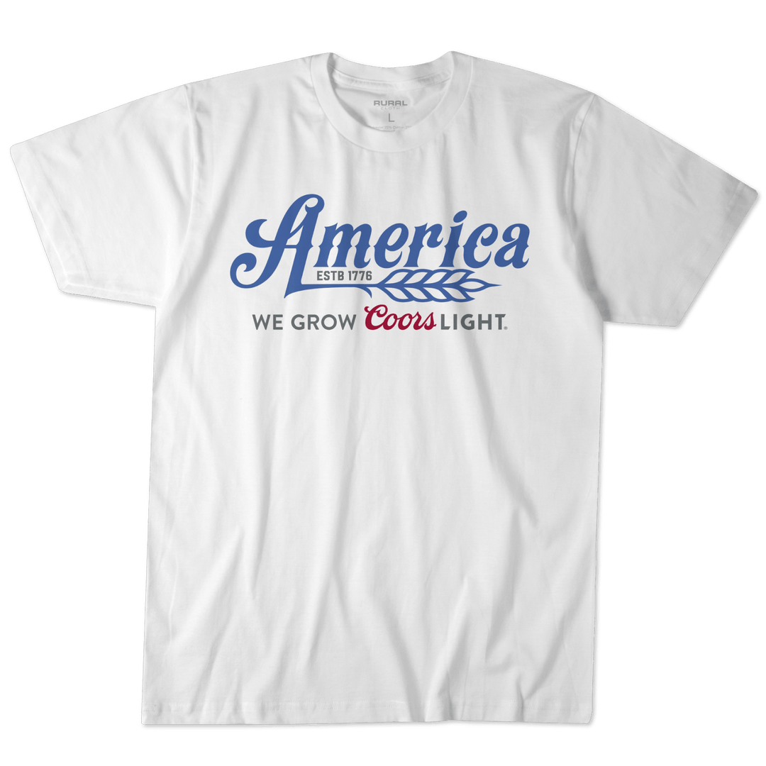 A white t-shirt from Rural Cloth, named the "We Grow Coors Light Tee," features blue text declaring "America ESTB 1776" accompanied by a wheat graphic. Below, it proudly reads "We Grow Coors Light" in black and red, celebrating the legacy of this iconic American beer.