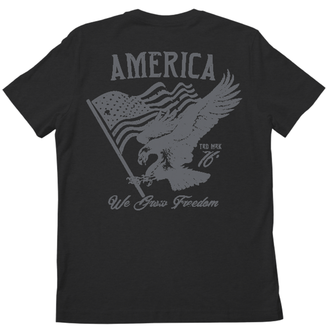 The Rural Cloth We Grow Freedom Tee is a black patriotic shirt with a graphic on the back featuring an American eagle clutching a tattered American flag. Above the eagle, "AMERICA" is printed in large letters, and below, the phrase "We Value Freedom" is written.