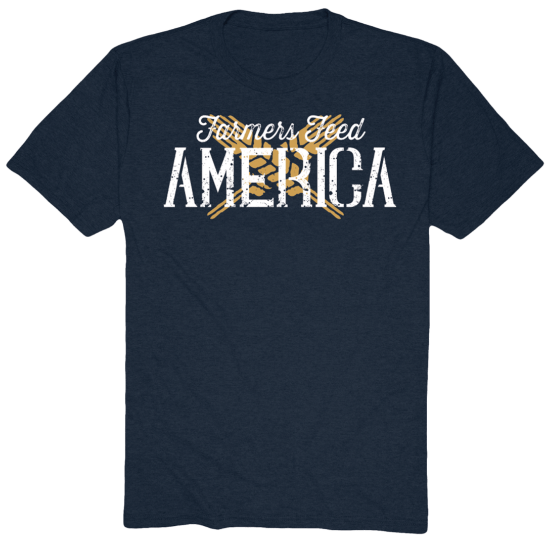 The Wheat X Tee-Heather Navy by Rural Cloth showcases a dark blue T-shirt with the white text "Farmers Feed AMERICA" in a faded style. It includes a design of two yellow crossed pitchforks behind the word "America." This iconic message is now also available on an olive green T-shirt featuring crossing wheat springs in the background.